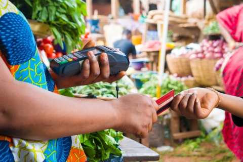 One person handing a credit card to another at a vegetable market