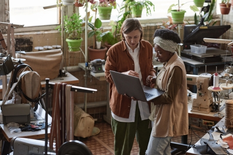 Two business women talk, with one holding a laptop.