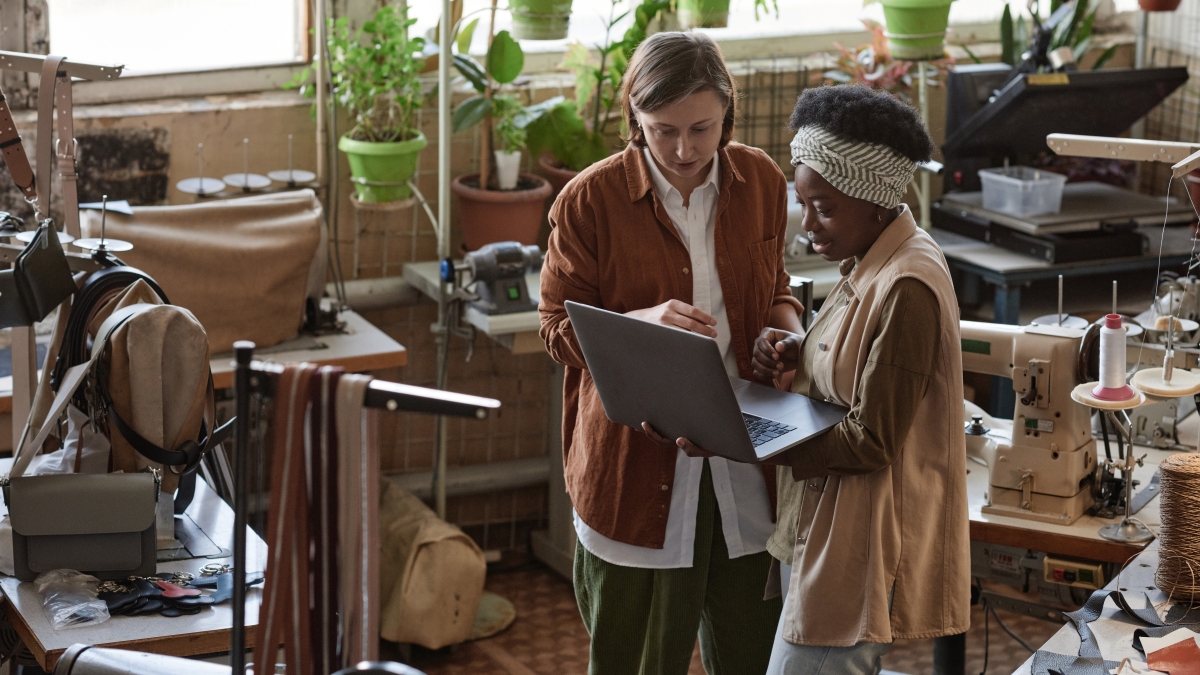 Two business women talk, with one holding a laptop.